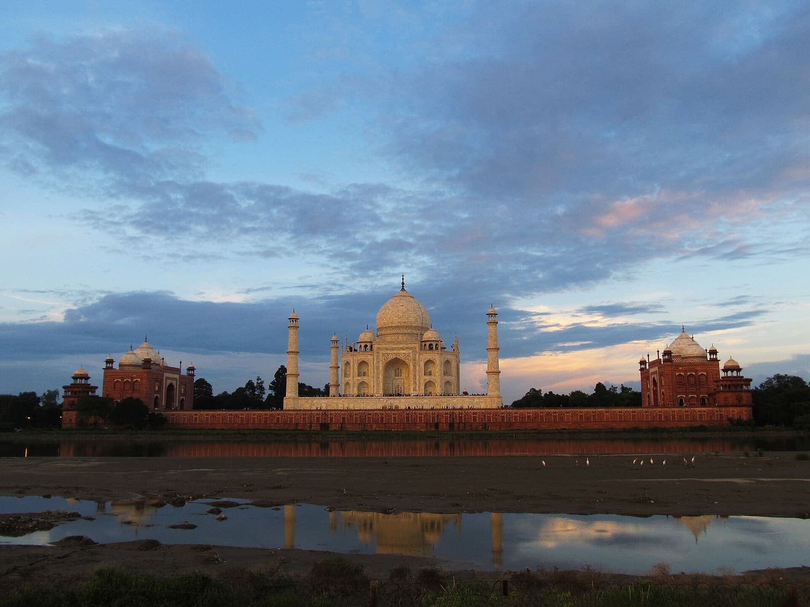The Taj Mahal at sunset, seen across the Yamuna from the Mehtab Bagh side, with its red sandstone mosque and guest house either side