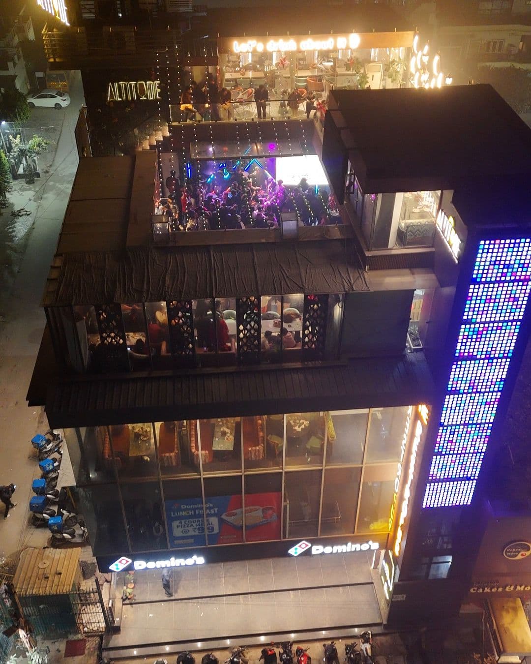 The Altitude building from the air on New Year’s Eve 2025: both levels of the roof lit and full of guests, Domino’s at street level
