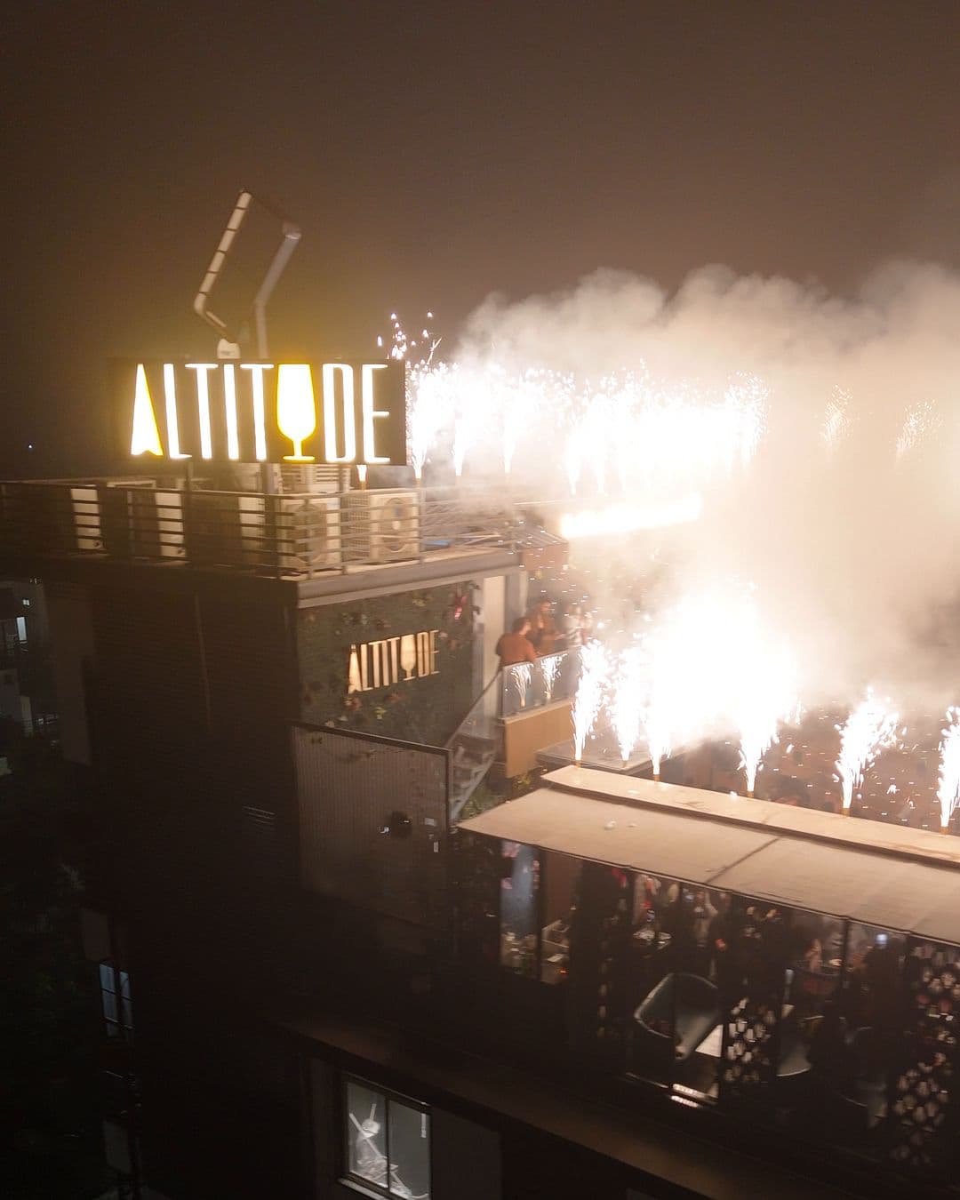 The lit ALTITUDE sign on the roof with fireworks and smoke beside it at midnight, New Year’s Eve 2025