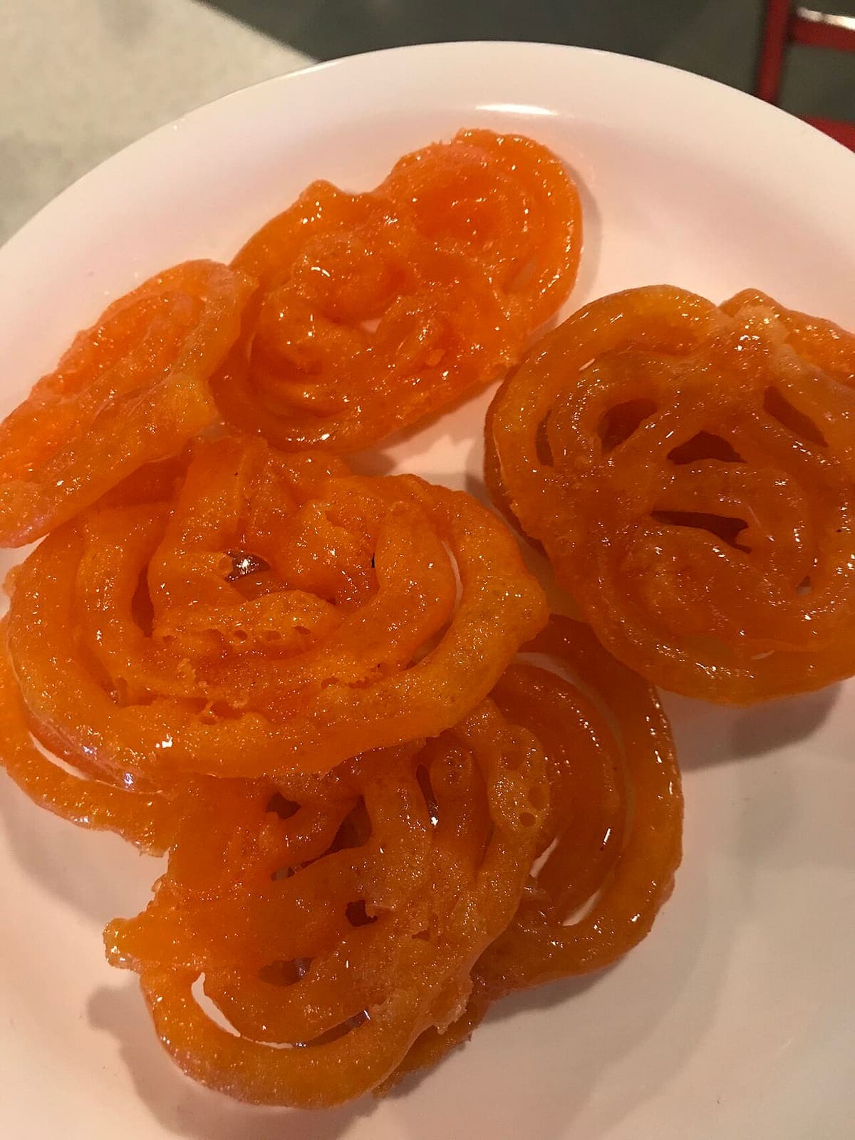 Close-up of glossy orange jalebis, the coiled sweet soaked in sugar syrup