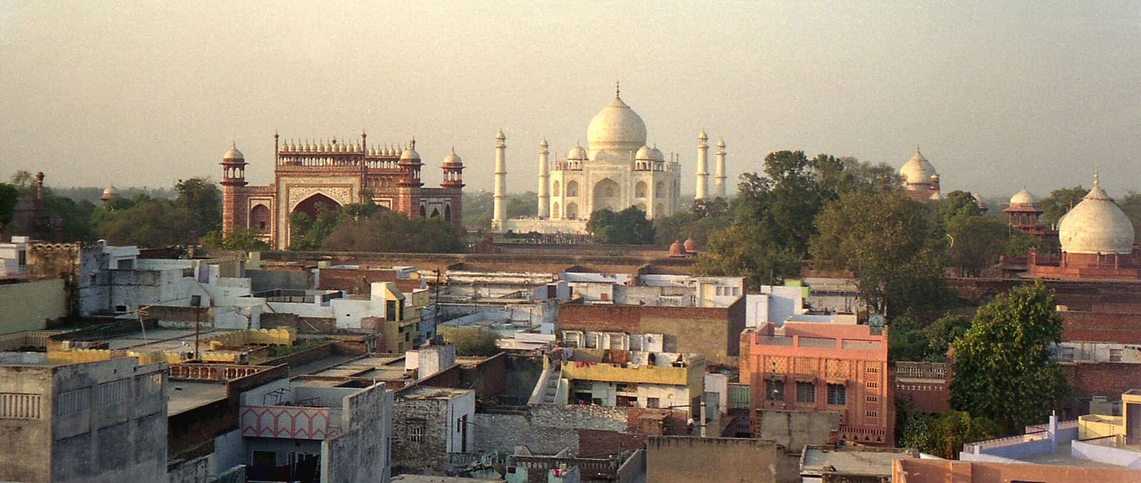 Panorama over the flat rooftops of Taj Ganj, with the Taj Mahal and its red sandstone gateway rising behind