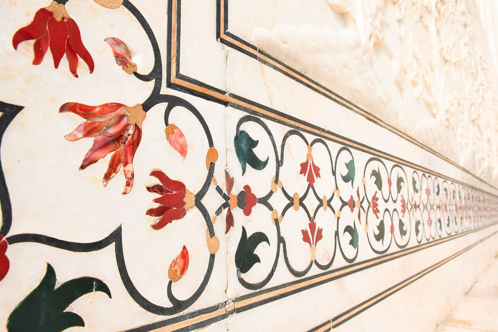 Red, orange and dark green stone flowers and vines inlaid in the white marble of the Taj Mahal