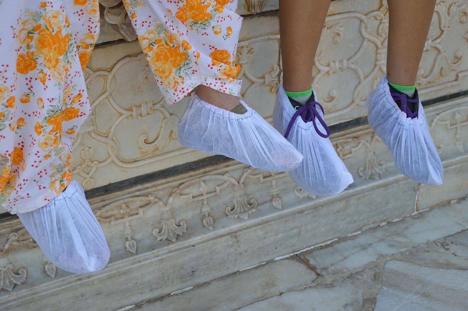 Visitors’ feet in white fabric shoe covers resting on the carved marble of the Taj Mahal’s plinth